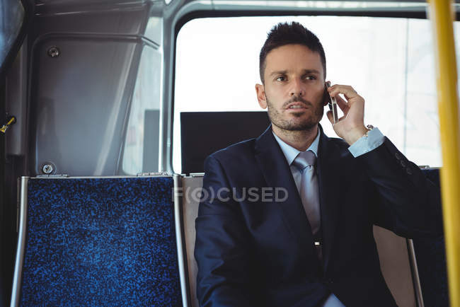 Бизнесмен разговаривает по мобильному телефону во время поездки на автобусе — стоковое фото