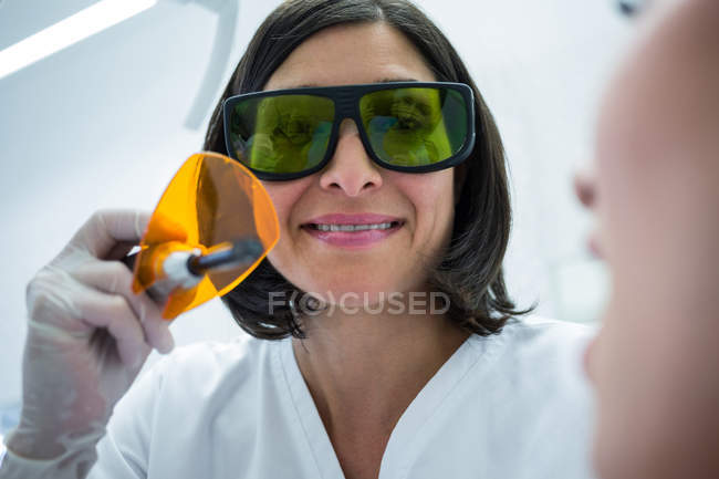 Врач-стоматолог осматривает зубы молодых пациентов при помощи света для лечения зубов в клинике — стоковое фото