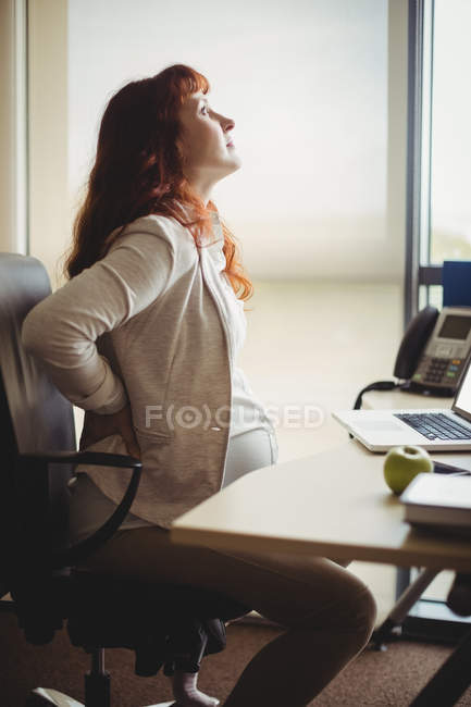 Pregnant businesswoman holding back while sitting on chair in office — Stock Photo