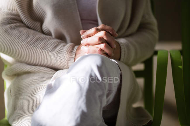Seção média da mulher sênior sentada com as mãos apertadas — Fotografia de Stock