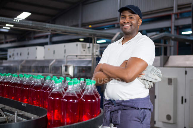 Portrait de travailleur masculin avec les bras croisés debout par des bouteilles sur la chaîne de production dans l'usine — Photo de stock
