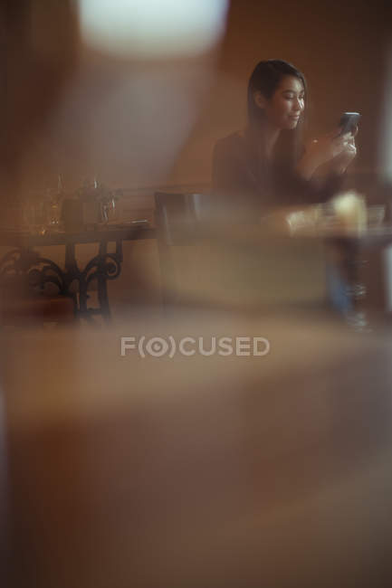 Mulher sorridente usando telefone celular no café — Fotografia de Stock