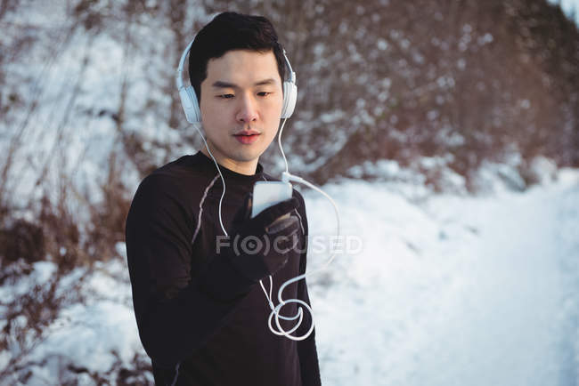 Чоловік слухає музику в навушниках зі смартфона взимку — стокове фото