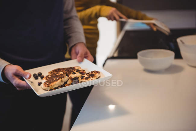 Homem segurando bandeja de biscoitos na cozinha em casa — Fotografia de Stock