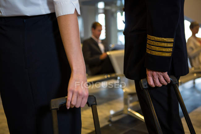 Secção intermédia do piloto e hospedeira aérea segurando seus sacos de carrinho na área de partida — Fotografia de Stock