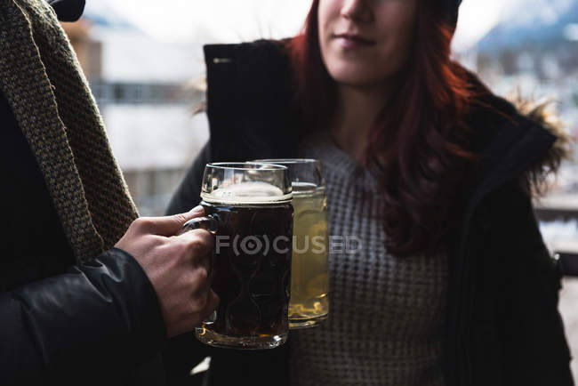 Primer plano de amigos sosteniendo vasos de cerveza en la terraza al aire libre - foto de stock