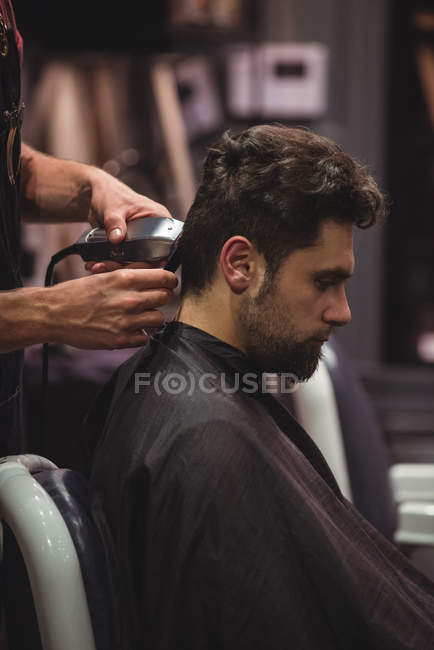 Hombre consiguiendo pelo recortado por peluquería con trimmer en peluquería - foto de stock