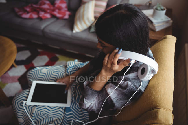 Femme écoutant de la musique avec écouteurs et tablette numérique dans le salon à la maison — Photo de stock