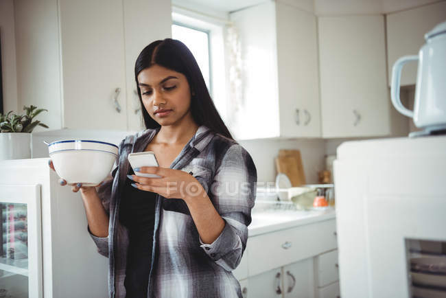 Женщина с мобильного телефона во время завтрака на кухне дома — стоковое фото