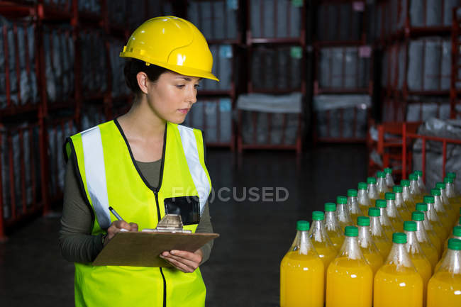Молода жінка-працівник вивчає пляшки соку на заводі — стокове фото