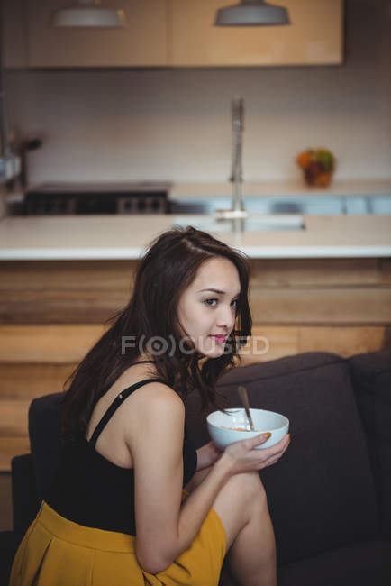 Woman sitting on sofa eating breakfast cereal in living room at home — Stock Photo