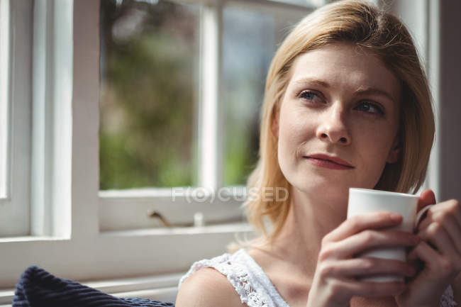 Thoughtful woman having coffee in living room at home — Stock Photo