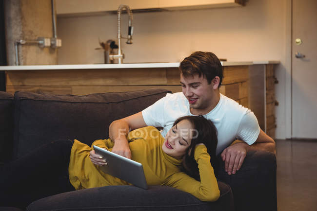 Couple joyeux couché ensemble sur le canapé en utilisant une tablette numérique dans le salon — Photo de stock