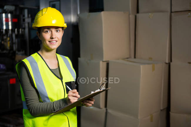 Portrait of female worker writing on clipboard in warehouse — Stock Photo