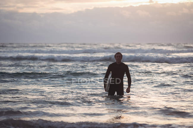 Porträt eines Mannes mit Surfbrett, der in der Abenddämmerung dem Meer entsteigt — Stockfoto