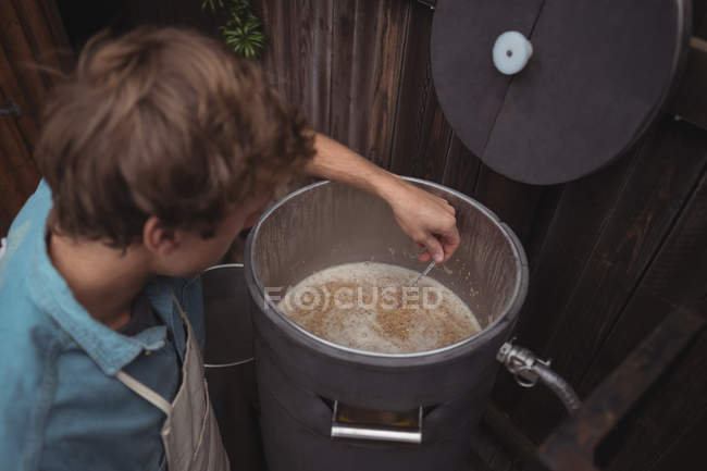 Homem testando a temperatura da cerveja em mosto ao fazer cerveja em casa cervejaria — Fotografia de Stock