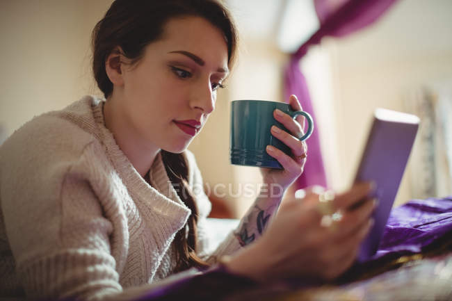 Mulher bonita usando tablet digital enquanto toma café na cama em casa — Fotografia de Stock