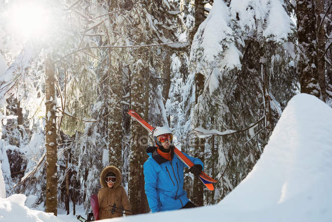 Couple avec ski et snowboard marchant sur une pente enneigée — Photo de stock