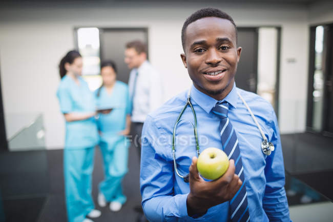 Портрет усміхненого лікаря, який тримає зелене яблуко в лікарняному коридорі — стокове фото