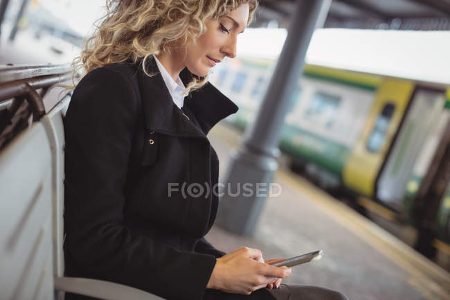 Side view of businesswoman text messaging at bench at railroad station — Stock Photo