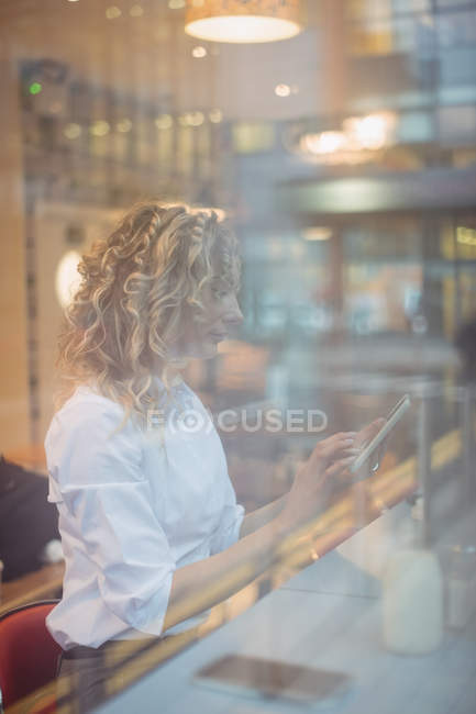 Mujer de negocios reflexivo uso de tableta digital en el mostrador en la cafetería - foto de stock