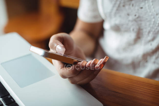 Sección media de la mujer usando el teléfono móvil en la cafetería - foto de stock