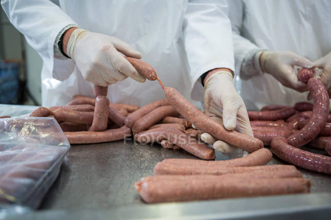 Corte médio de açougueiros que processam salsichas na fábrica de carne — Fotografia de Stock
