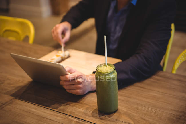 Businessman using digital tablet while having snack in cafe — Stock Photo