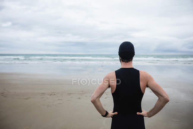 Sportler im Badeanzug steht mit Hand auf Hüfte am Strand — Stockfoto