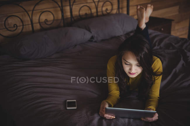 Femme couchée sur le lit en utilisant une tablette numérique dans la chambre à coucher à la maison — Photo de stock