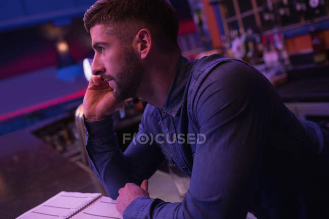 Bartender talking on mobile phone at counter in bar — Stock Photo