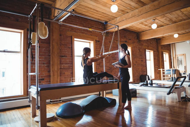 Formateur aidant femme tout en pratiquant pilates dans le studio de remise en forme — Photo de stock