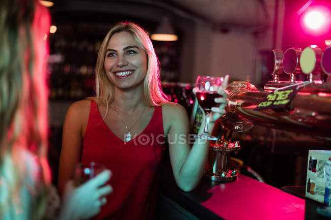 Mujeres interactuando mientras toman una copa de vino en el mostrador en el bar - foto de stock