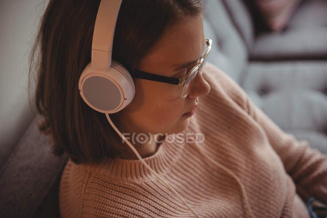 Жінка сидить на дивані слухає музику на навушниках у вітальні вдома — стокове фото