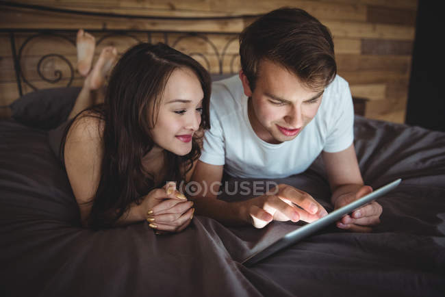 Пара лежа на кровати с помощью цифрового планшета в спальне дома — стоковое фото