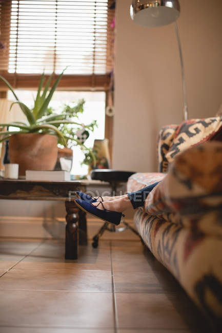 Jambes de fille assise sur le canapé dans le salon à la maison — Photo de stock