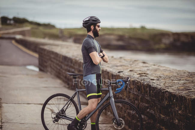 Спортсмен, стоящий с велосипедом на прибрежной дороге — стоковое фото