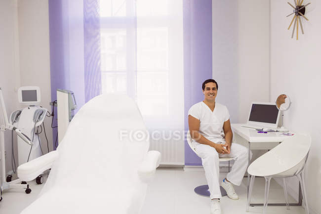 Mitte erwachsener lächelnder Arzt sitzt im Stuhl im Inneren der ästhetischen Klinik — Stockfoto