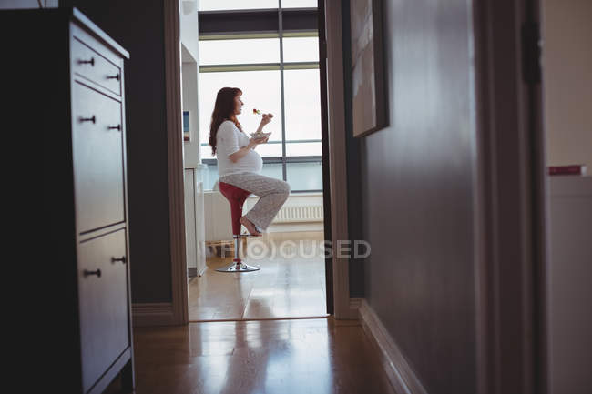 Schwangere sitzt auf Hocker und isst zu Hause Salat — Stockfoto