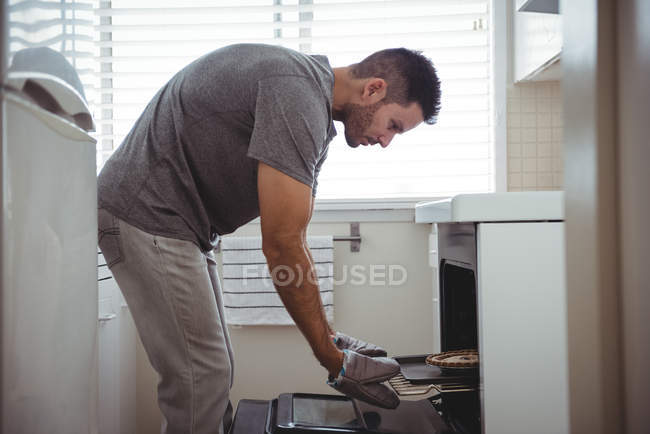Мужчина убирает пирог из духовки на кухне дома — стоковое фото