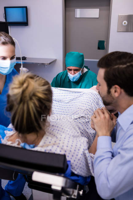 Медична команда вивчає вагітну жінку під час пологів, а чоловік тримає руку в операційній — стокове фото