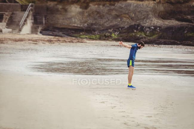 Bonito homem realizando exercícios de alongamento na praia — Fotografia de Stock