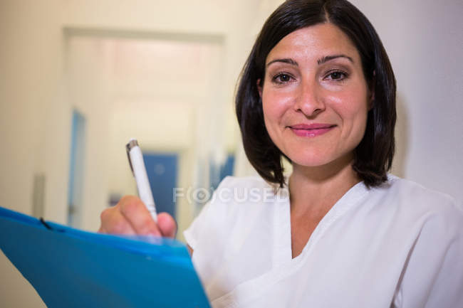 Retrato de un médico sonriente que examina el informe de los pacientes - foto de stock