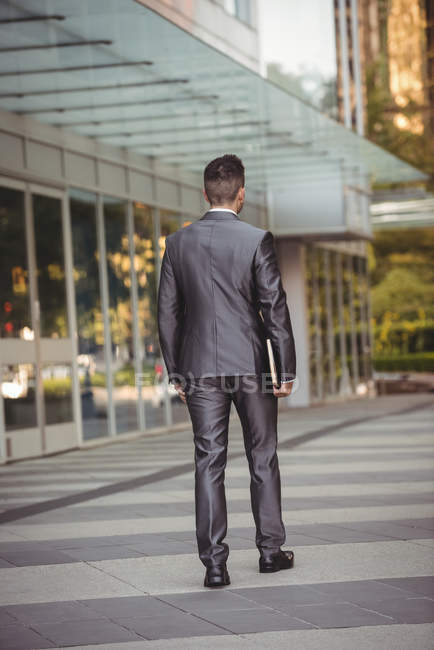 Vue arrière d'un homme d'affaires avec un journal marche dans le campus du bureau — Photo de stock