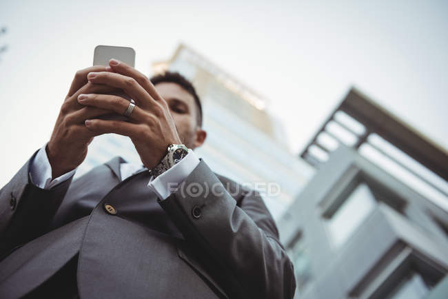 Vista a basso angolo di uomo d'affari utilizzando il telefono cellulare vicino all'edificio degli uffici — Foto stock