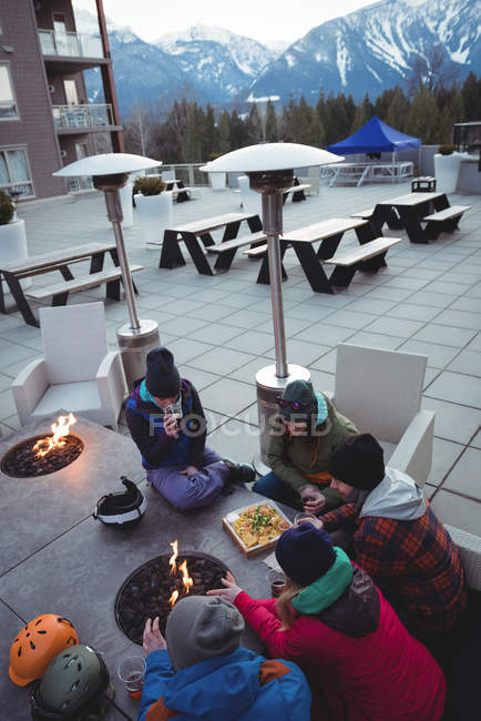 Group of skiers rubbing hands by fireplace in ski resort — Stock Photo