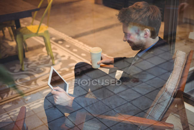 Empresário segurando copo de café descartável e usando tablet digital no café — Fotografia de Stock