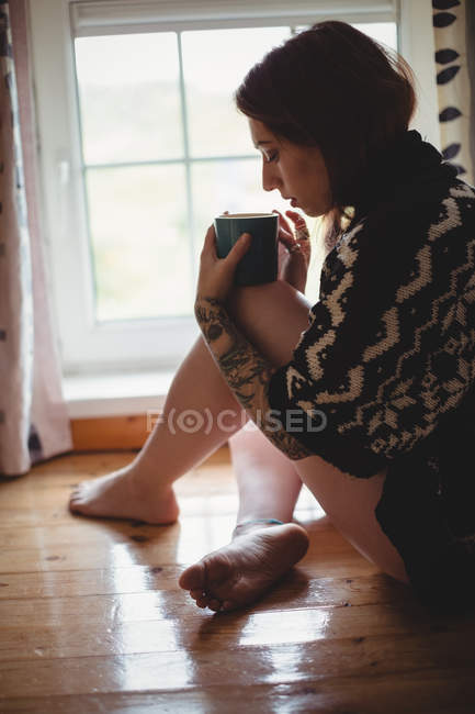 Woman sitting near window and having coffee at home — Stock Photo