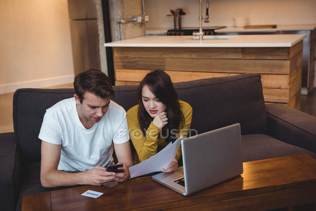 Casal sentado no sofá discutindo com documentos financeiros na sala de estar em casa — Fotografia de Stock
