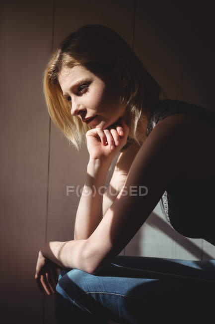 Mujer pensativa sentada con la mano en la barbilla en casa - foto de stock
